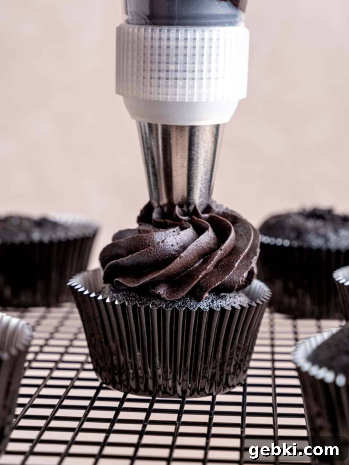 Piping black buttercream frosting onto a black cupcake with a large closed star tip.