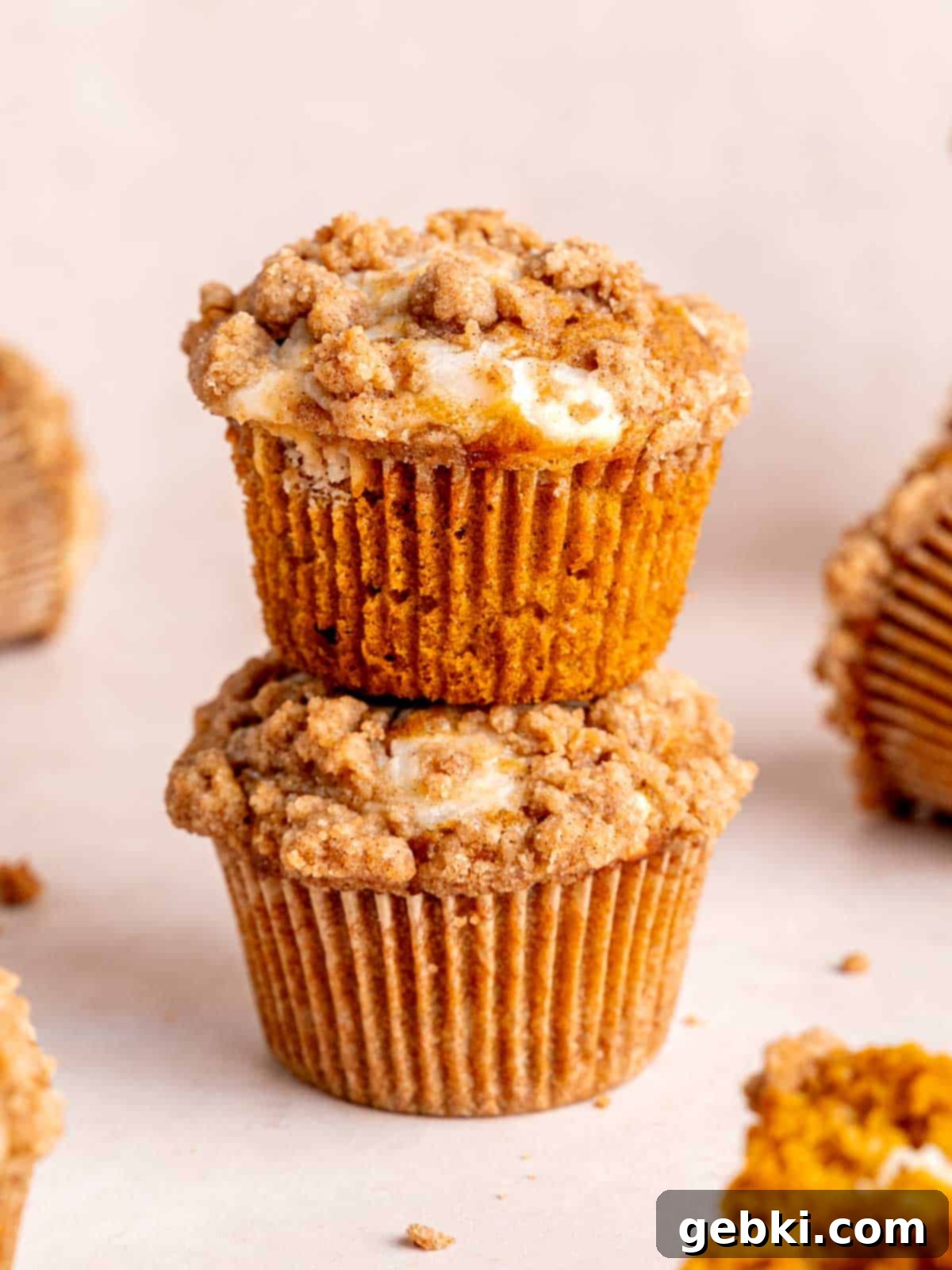 Two perfectly baked pumpkin cheesecake muffins, generously topped with cinnamon streusel, stacked elegantly to showcase their golden-brown tops and moist texture.