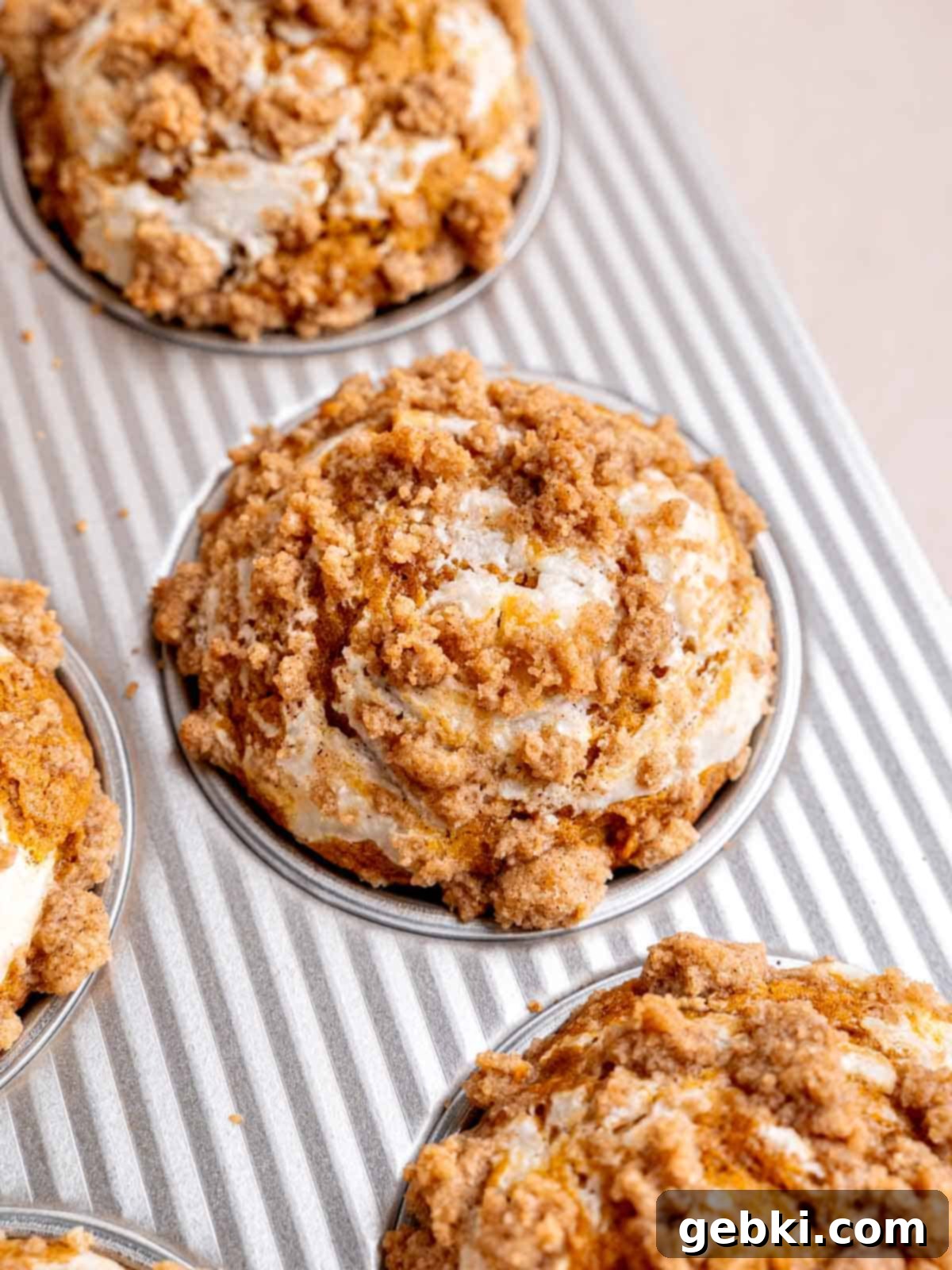 A fresh batch of pumpkin cream cheese muffins with a golden streusel topping, baked to perfection in a muffin pan.