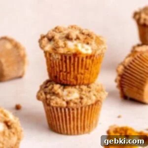 A stack of perfectly baked pumpkin cheesecake muffins, topped with a golden cinnamon streusel, ready to be enjoyed.