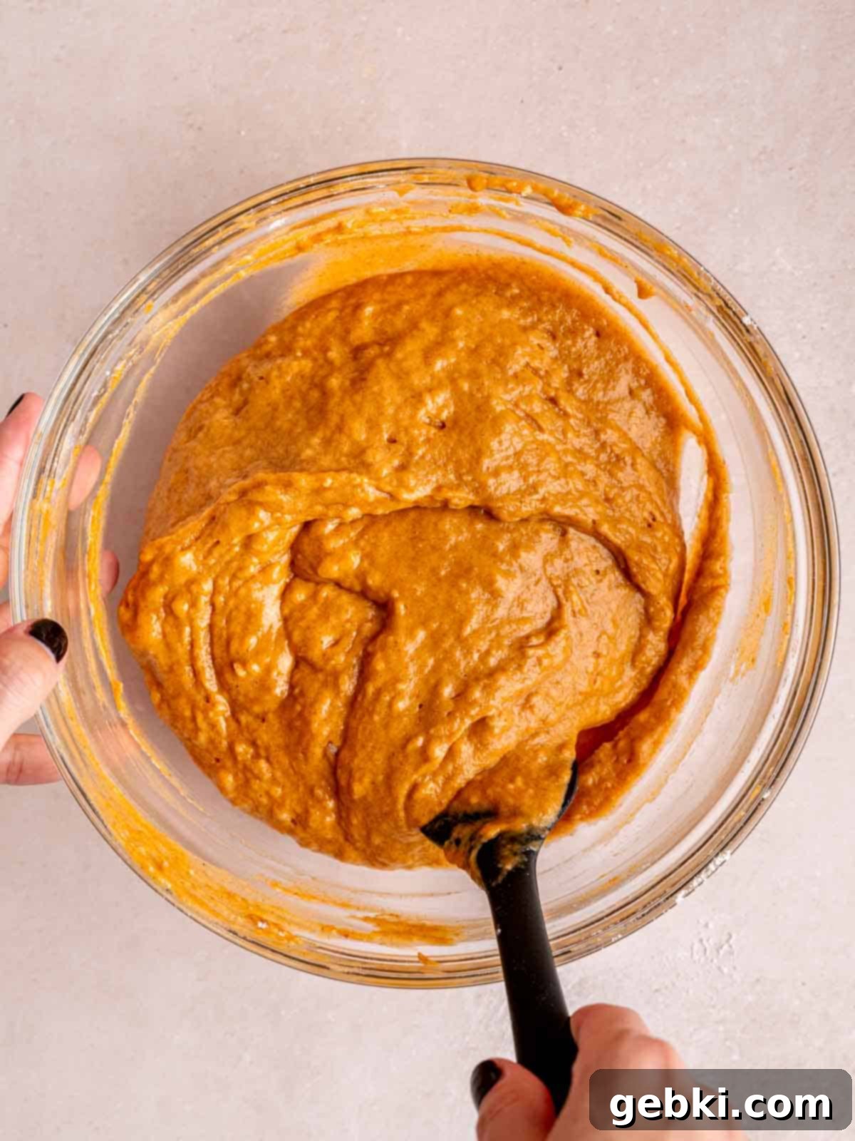 A rubber spatula gently folding the dry ingredients into the wet pumpkin muffin batter, ensuring a perfectly mixed yet tender consistency.
