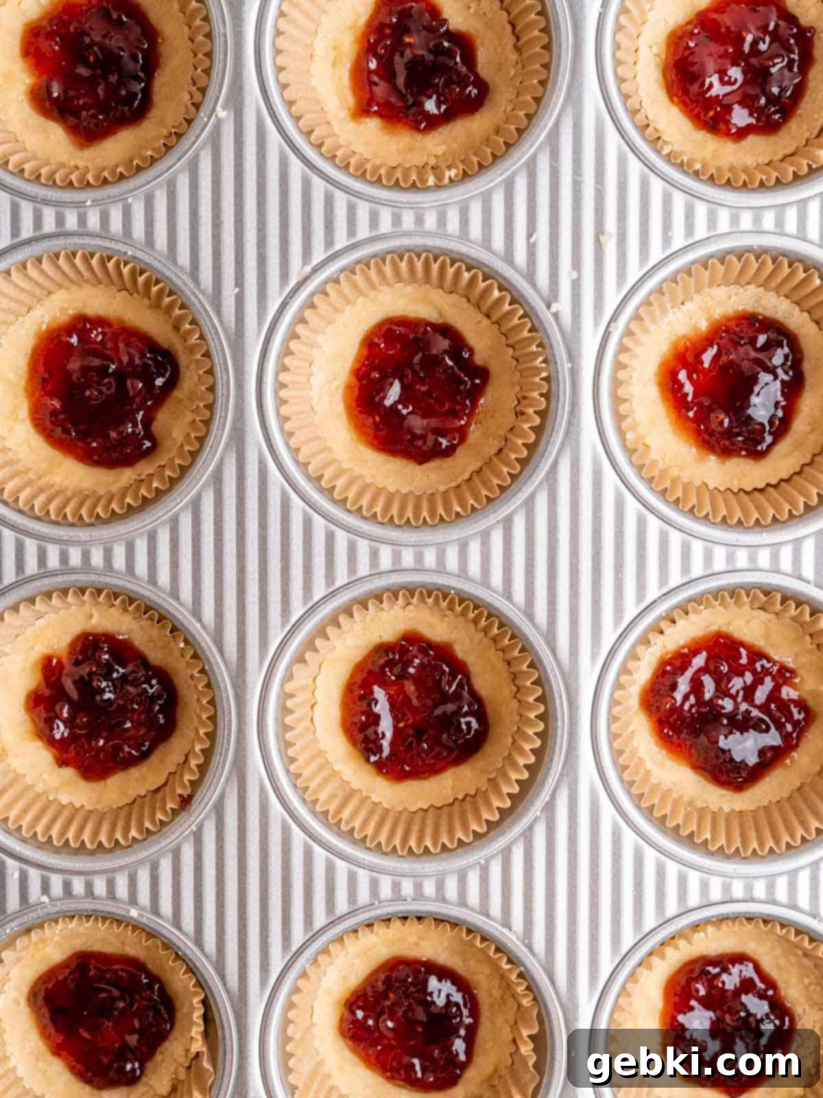 Simply Superior Easy Raspberry Crumble Cookies 7 Cookie dough bases in muffin liners with a dollop of vibrant red raspberry jam on top.