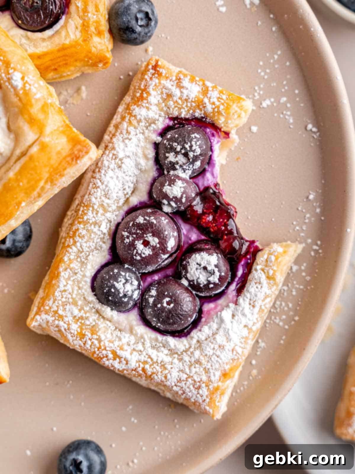 A blueberry cheese danish puff pastry with a bite taken out of it, showing flaky layers and creamy filling.