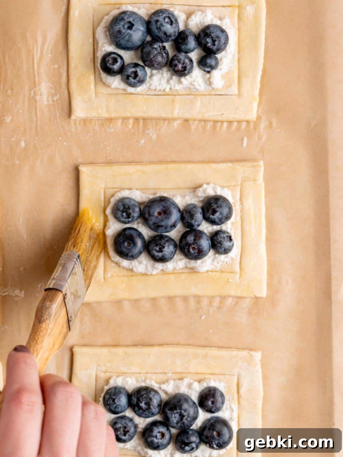 Simple Blueberry Cream Cheese Puffs 7 Brushing egg wash over the edges of puff pastry rectangles before baking.
