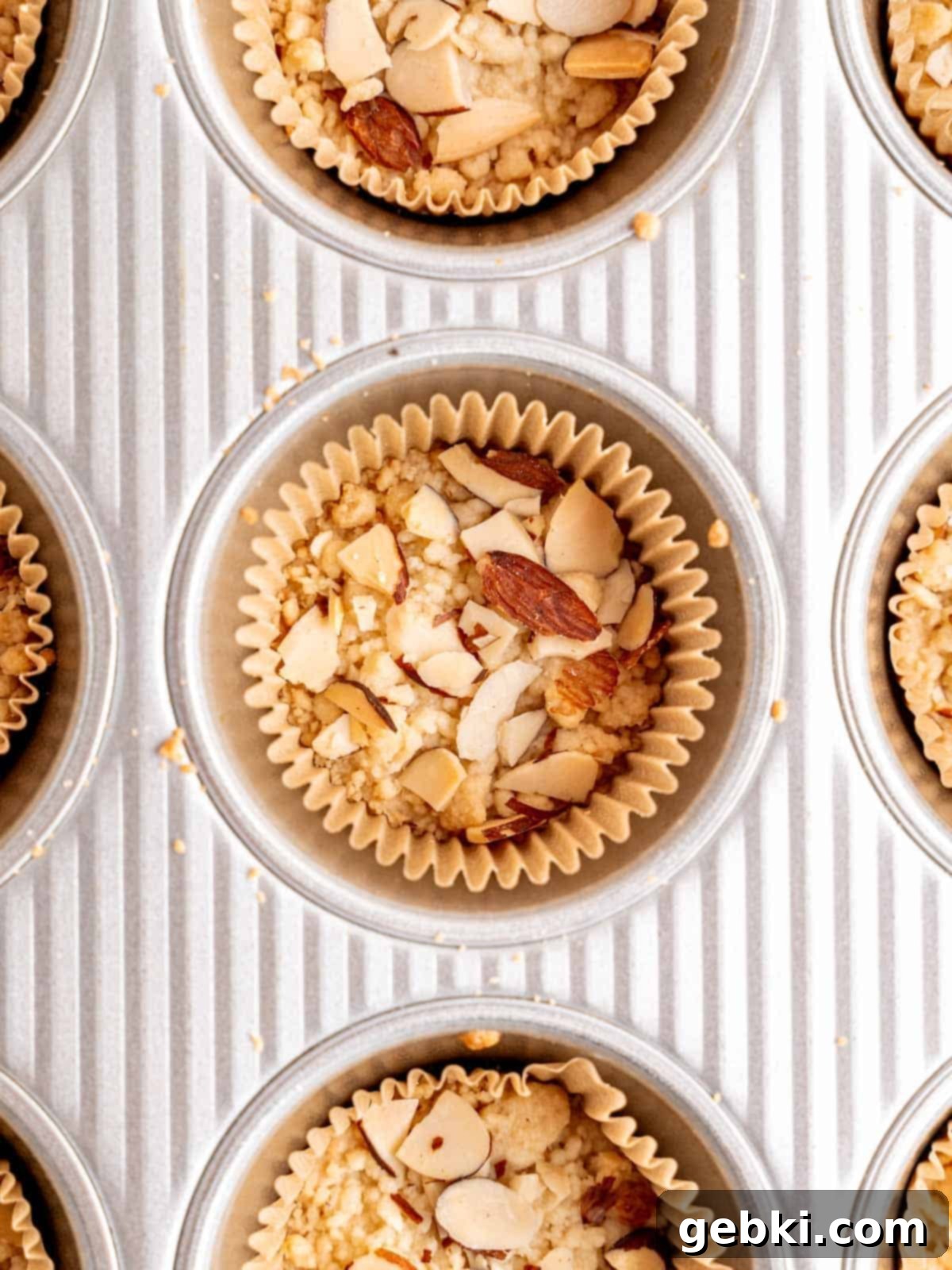 Baked shortbread cookies with golden-brown crumb topping and sliced almonds, cooling in a muffin pan after baking.