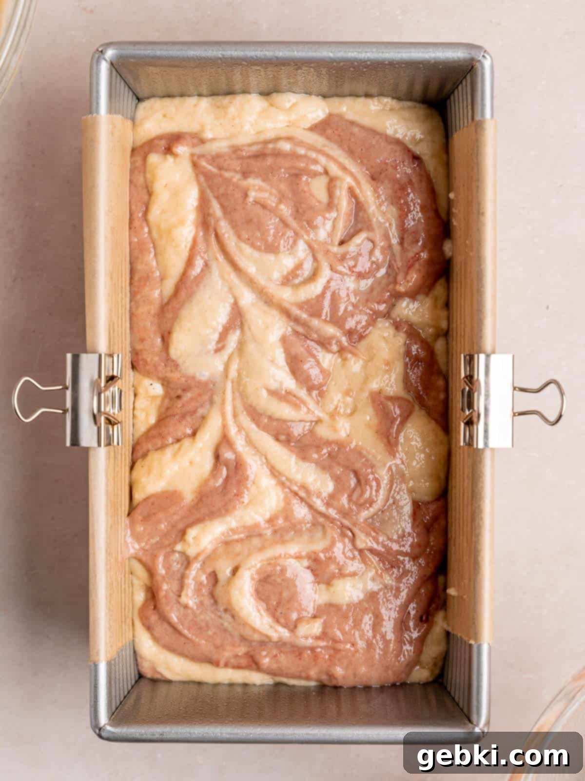 A loaf pan filled with swirls of vanilla and strawberry cake batters.