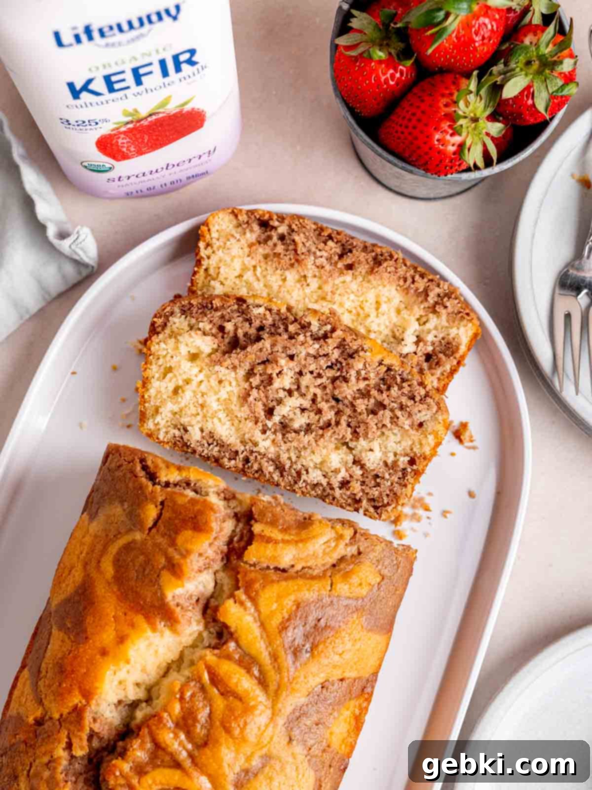 A strawberry swirl loaf cake sliced up on a plate next to a bottle of Lifeway Strawberry Kefir.