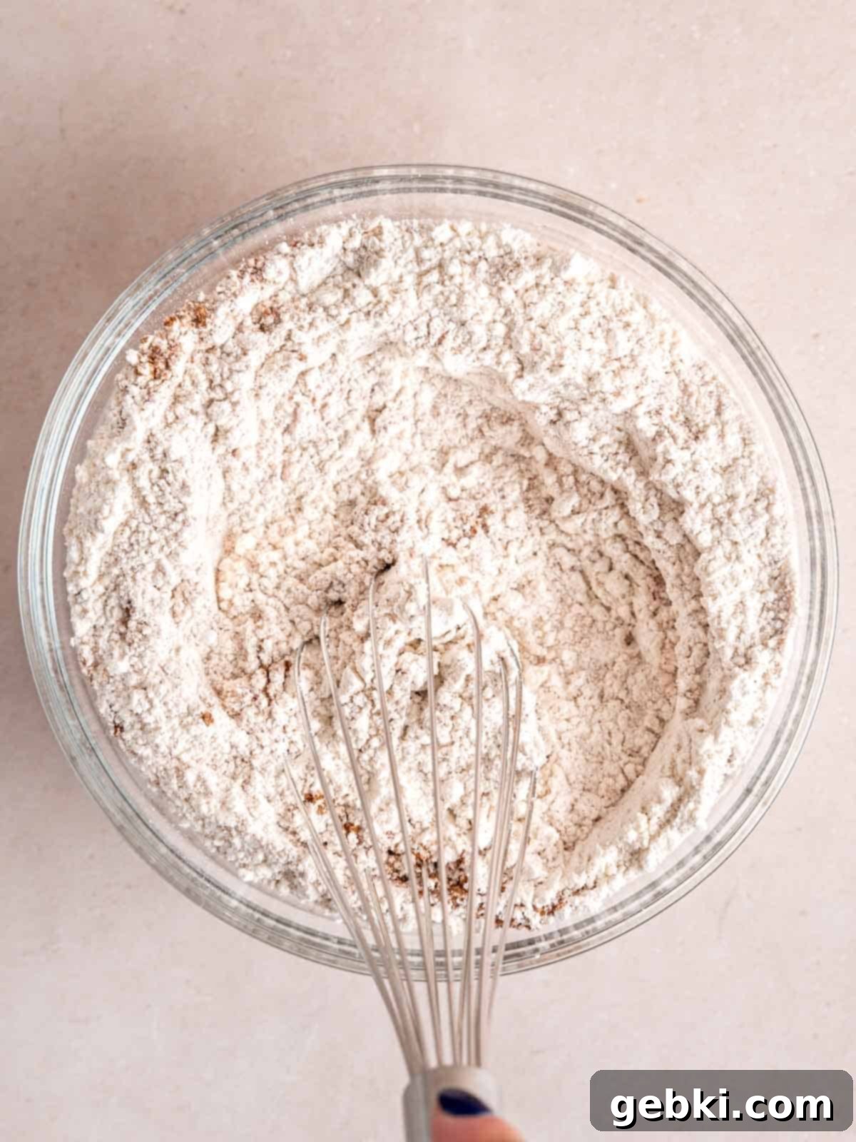 Whisking flour, baking powder, salt, and cinnamon together in a bowl, ensuring even distribution of dry ingredients.
