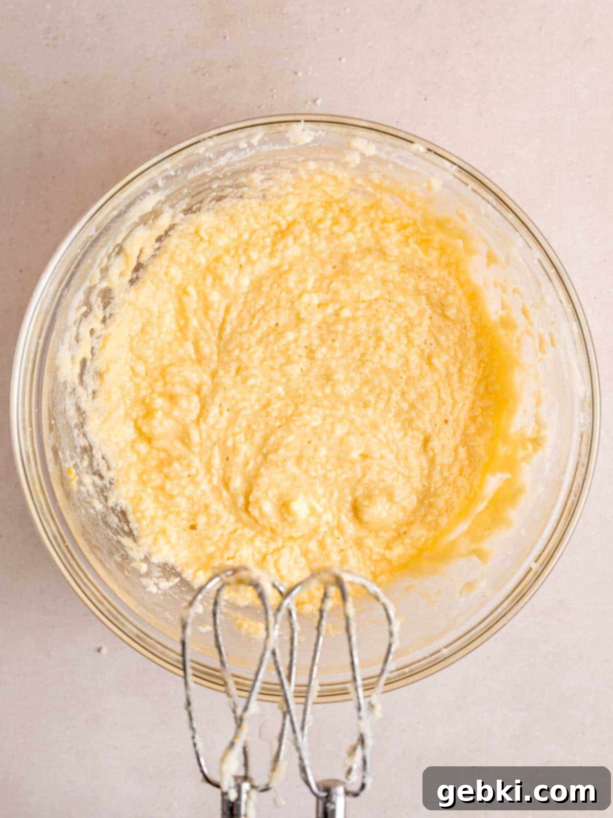 Butter, sugar, eggs, and vanilla extract mixed together in a bowl using an electric hand mixer, creating a light and fluffy wet mixture.