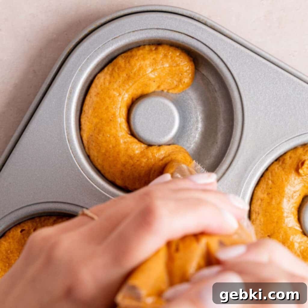Piping pumpkin batter into a greased metal donut pan for baking.