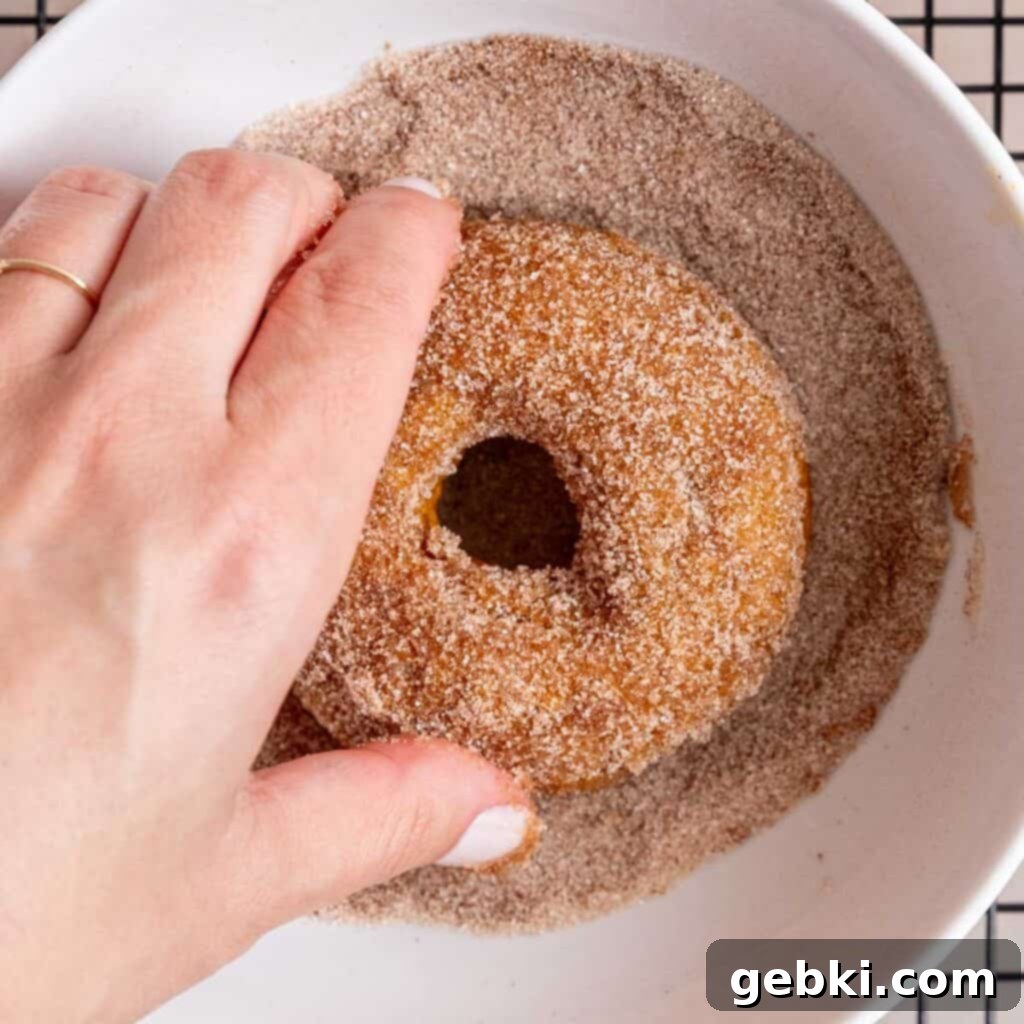 Coating a baked pumpkin donut in a bowl of cinnamon sugar mixture.