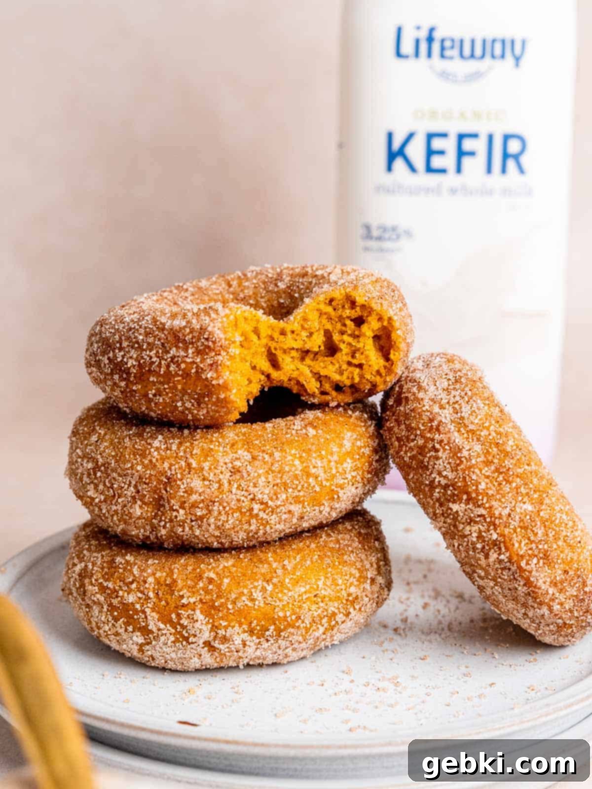 A stack of perfectly baked pumpkin donuts, with one donut showing a bite taken out, coated in cinnamon sugar.