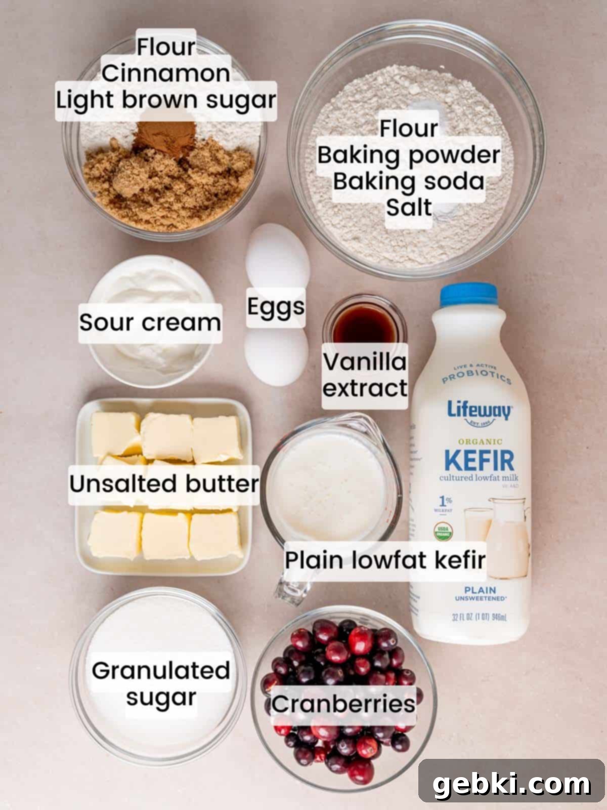 Quick Cranberry Coffee Cake 3 A collection of essential baking ingredients laid out on a wooden surface, including fresh cranberries, butter, granulated sugar, flour, Lifeway kefir, sour cream, and vanilla extract, ready to be combined for the cranberry coffee cake.