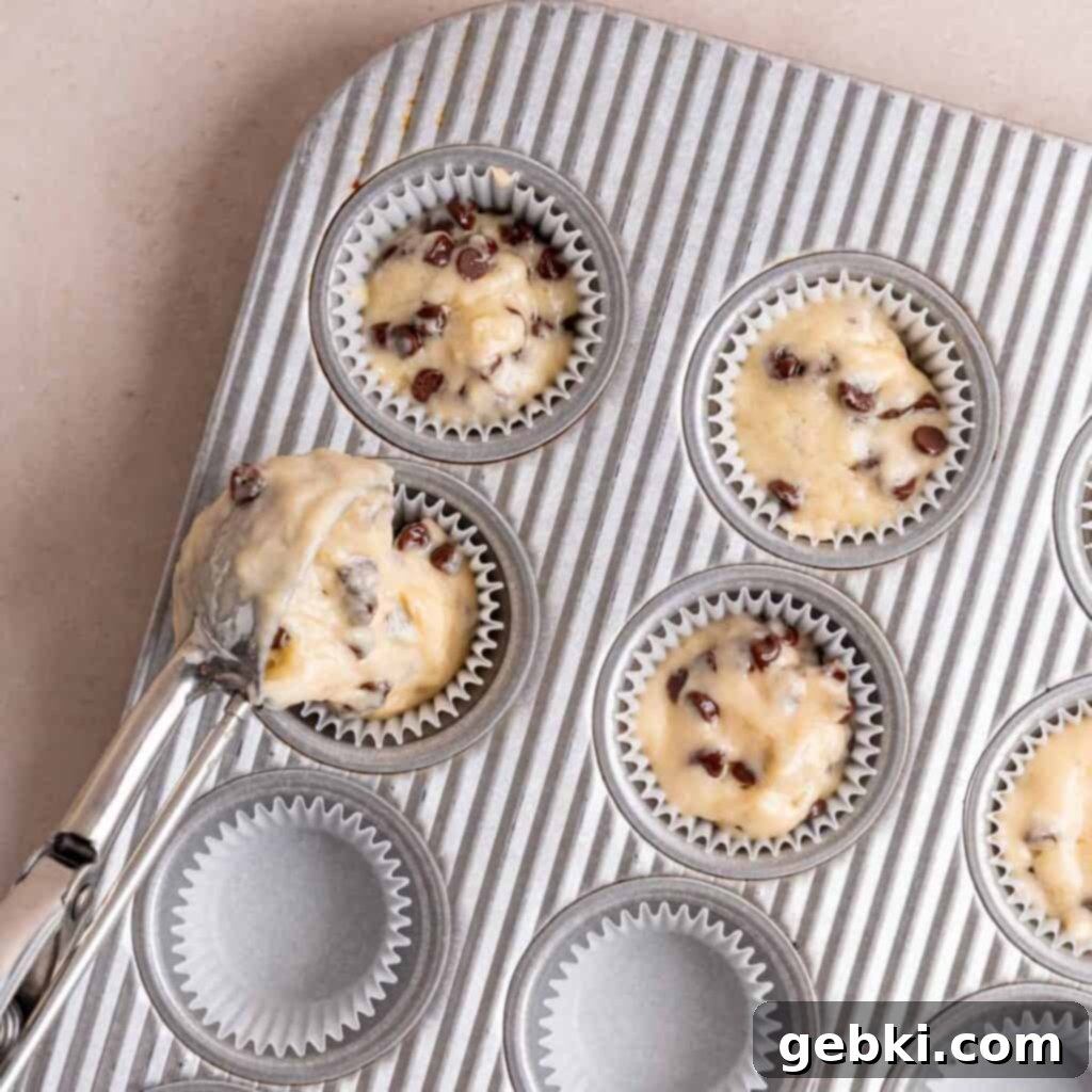 Scooping chocolate chip batter into a mini muffin pan.
