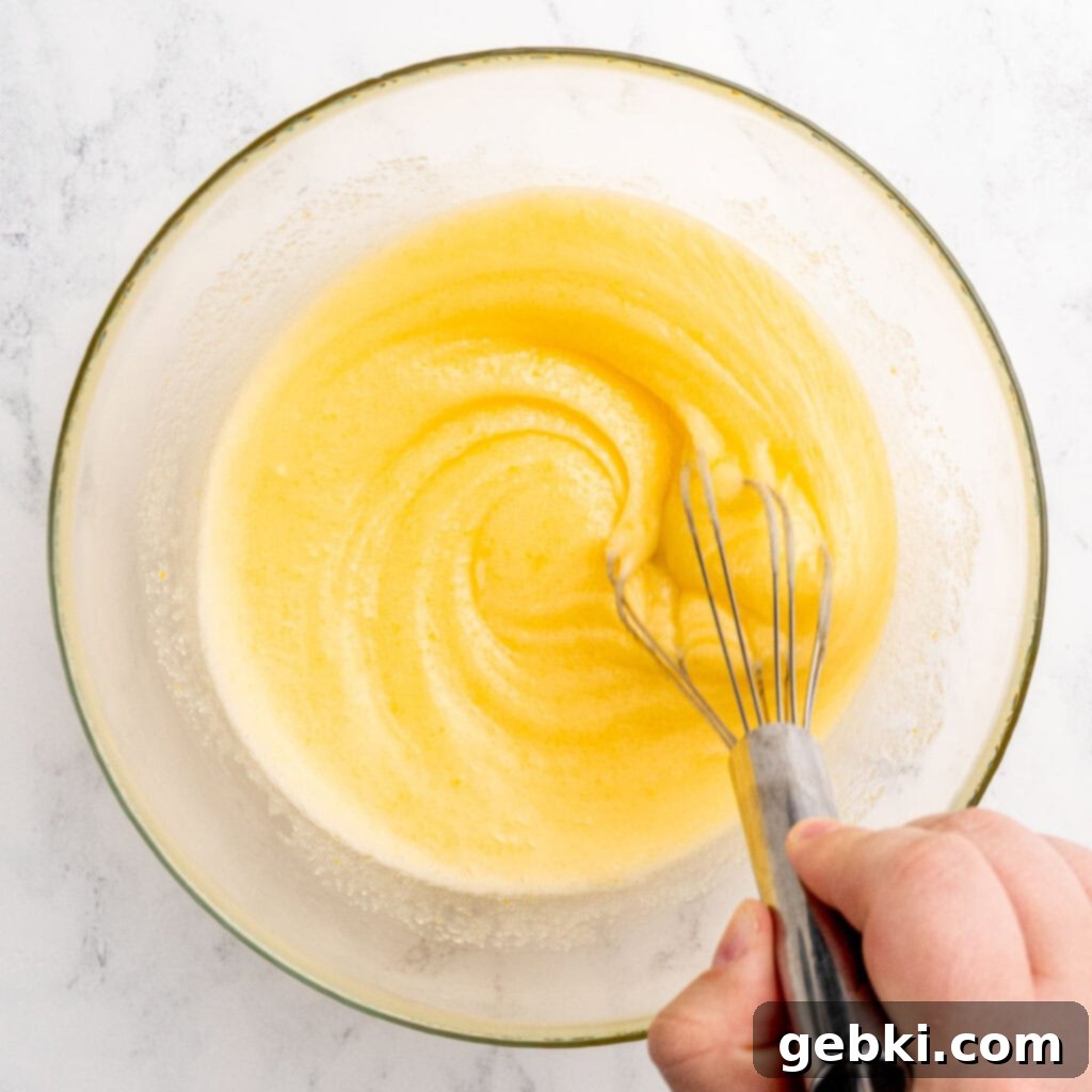 Whisking melted butter, granulated sugar, vanilla extract, and an egg in a bowl.