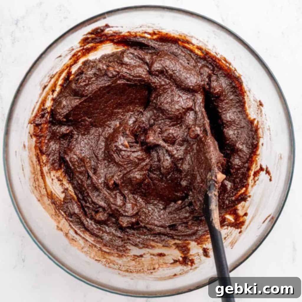 A small batch of brownie batter with chocolate chips in a bowl with a spatula.