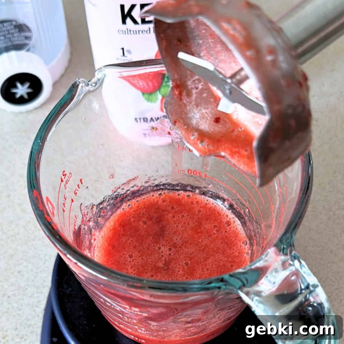 Strawberry Matcha Ninja Creami Treat 4 Blending warm strawberries with sugar in a measuring cup with an immersion blender.