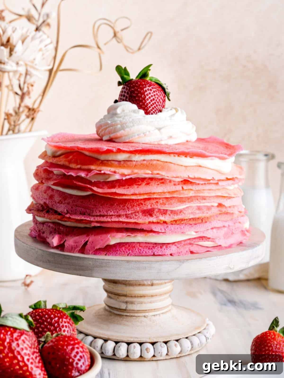 A beautifully layered strawberries and cream crepe cake topped with a dollop of whipped cream and a single fresh strawberry.
