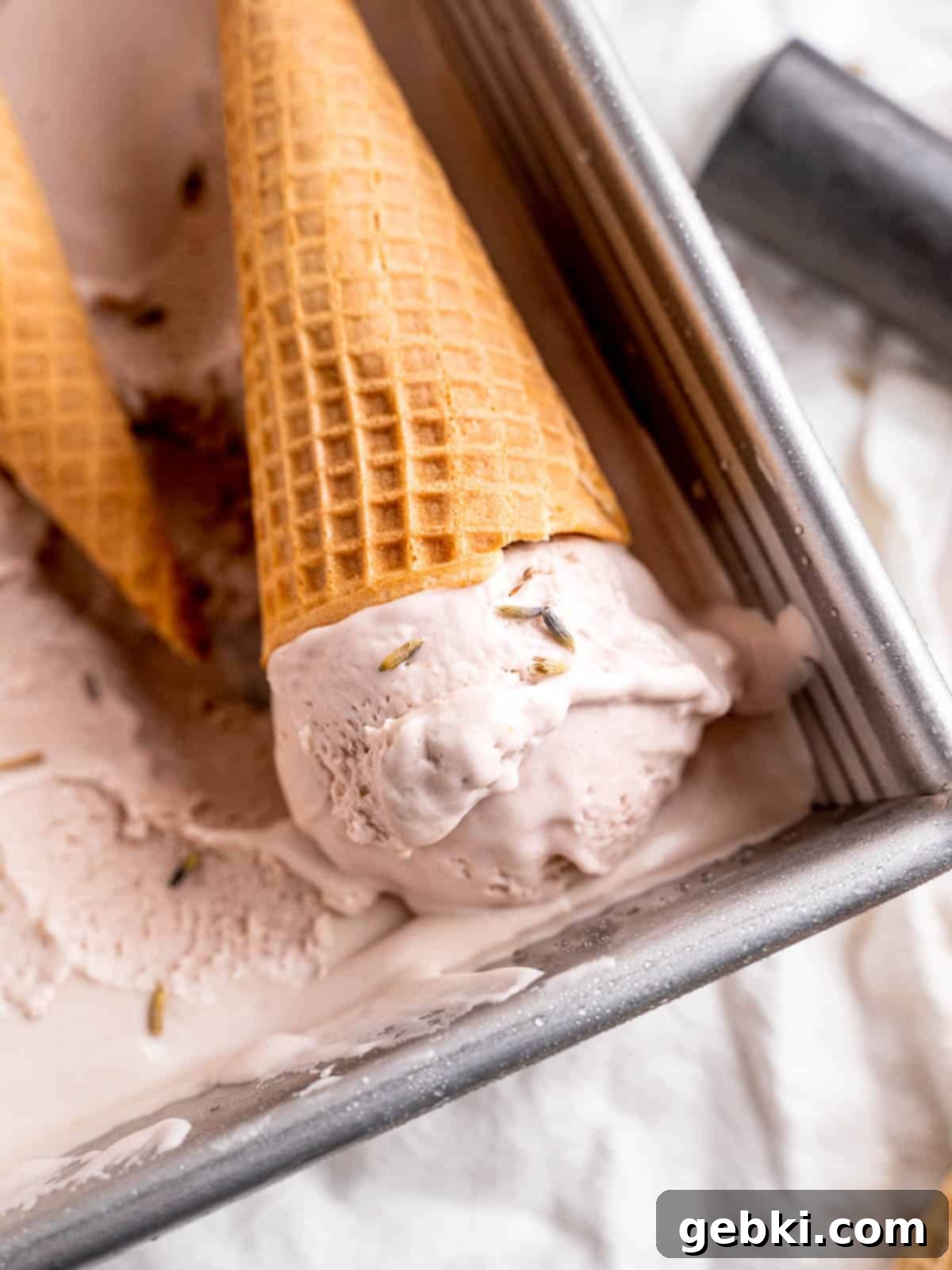 Lavender Honey Dream 2 A cone with a scoop of lavender honey ice cream laying in a pan of ice cream.