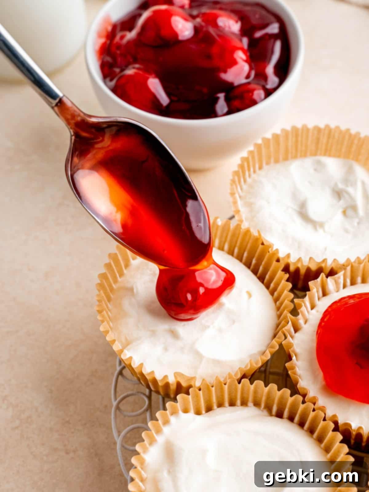 Adding cherry pie filling to the top of a no-bake mini cheesecake.