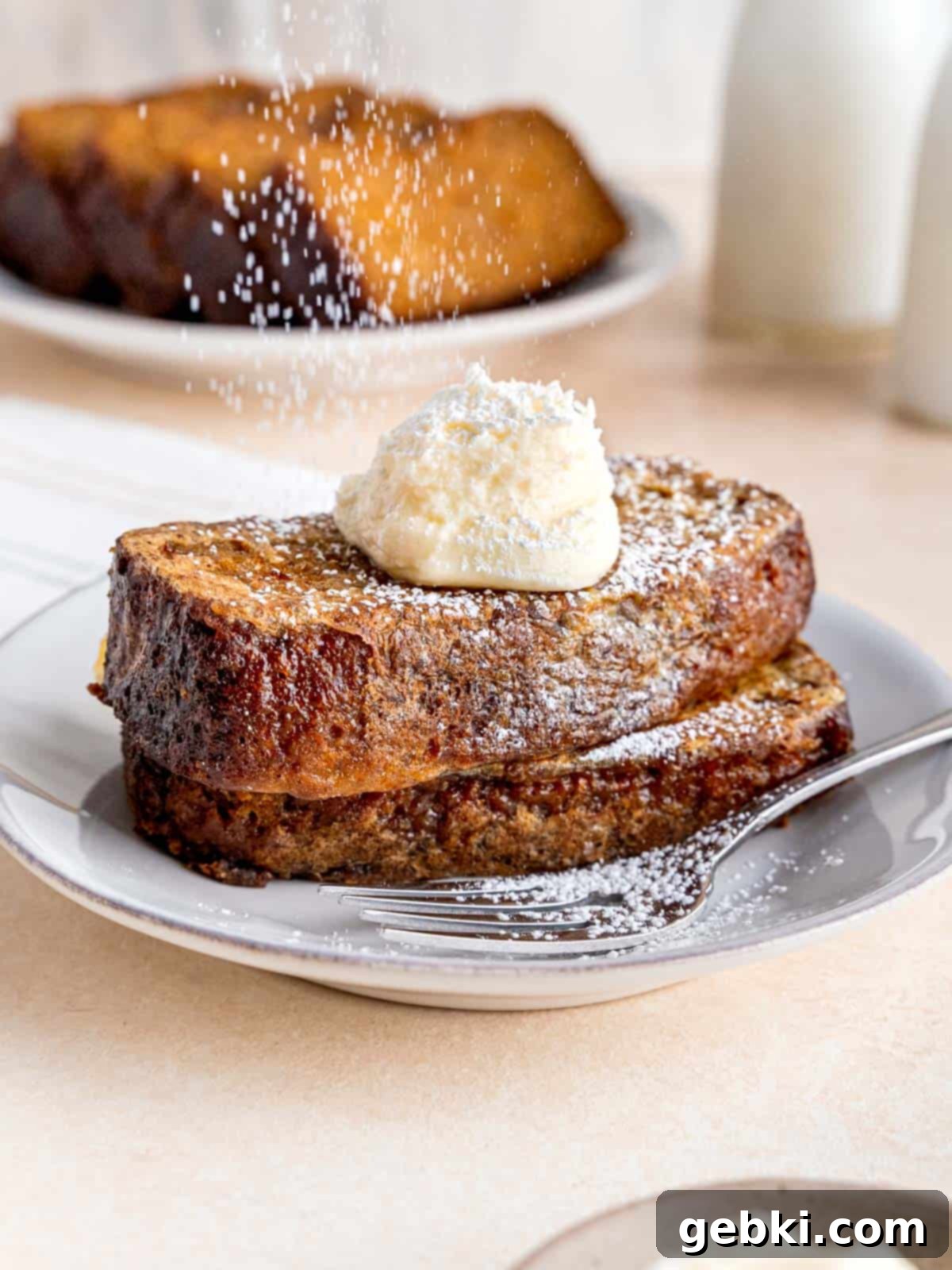 Sprinkling powdered sugar on top of 2 slices of carrot cake french toast.