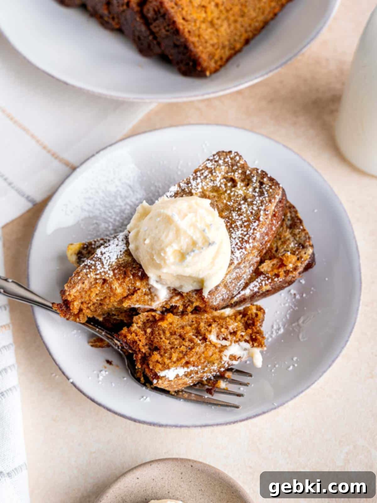 Two slices of carrot cake french toast with cream cheese frosting on a plate with a bite taken out of it.