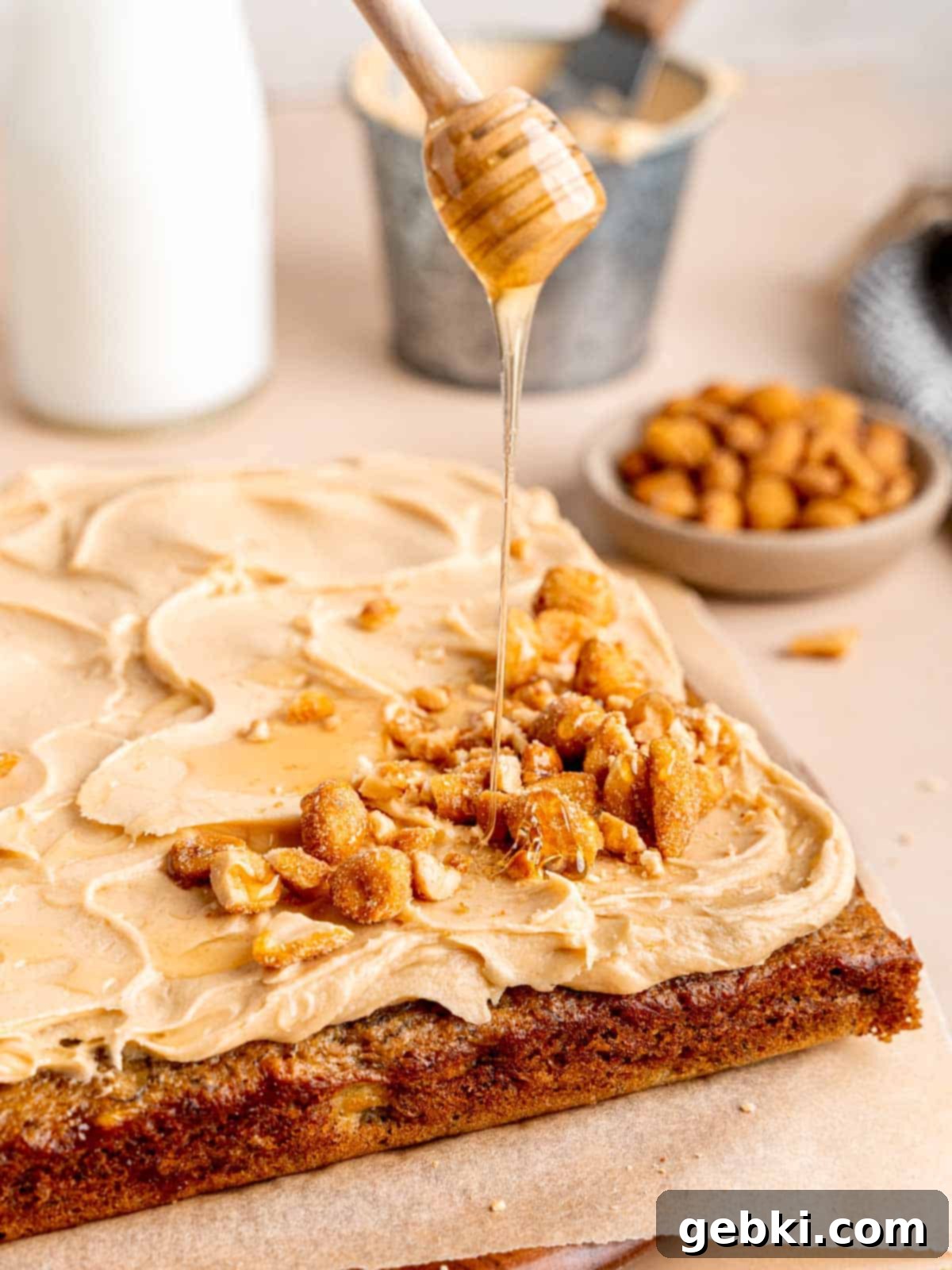 The Easiest Frosted Banana Cake Ever 8 Drizzling honey on top of a banana snack cake with peanut butter honey frosting.