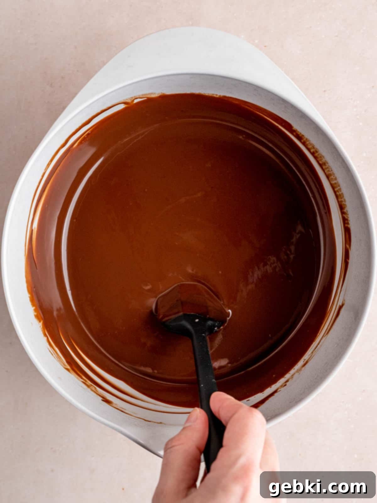 Banoffee Bliss Cupcakes 5 Stirring smooth chocolate ganache in a glass bowl with a rubber spatula.
