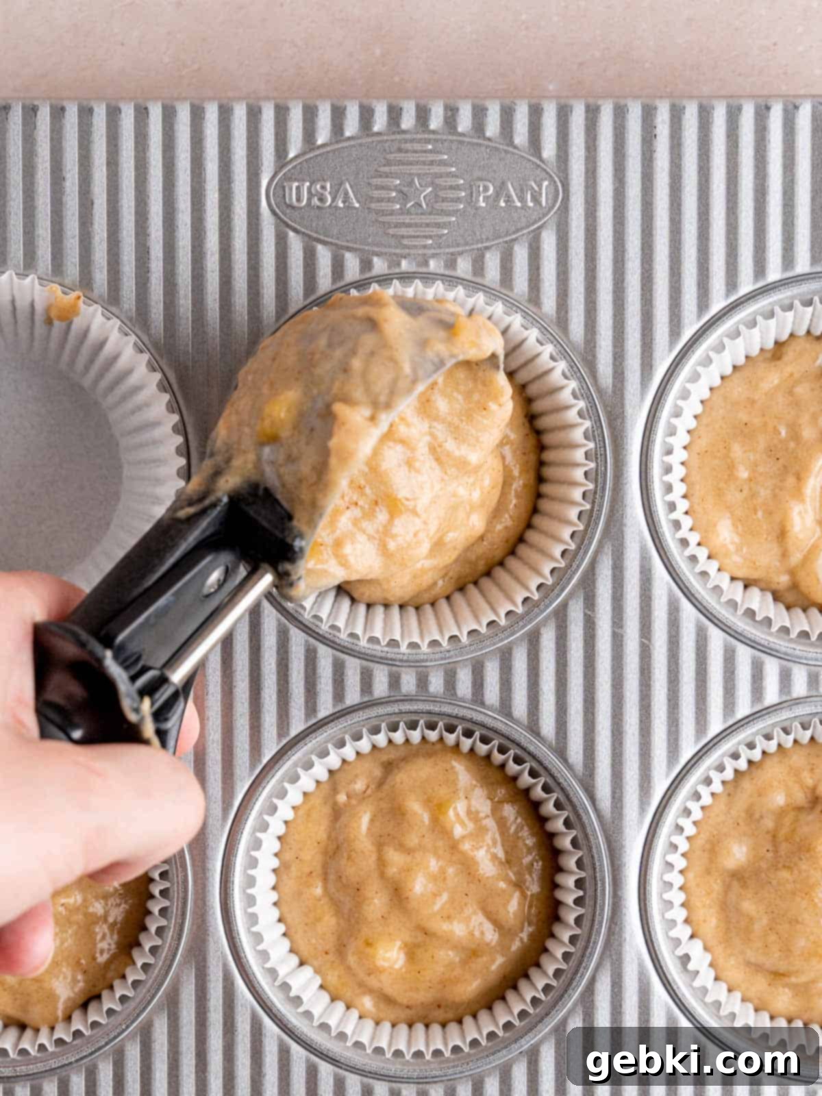 Banoffee Bliss Cupcakes 8 Scooping banana cupcake batter into paper liners in a muffin pan.