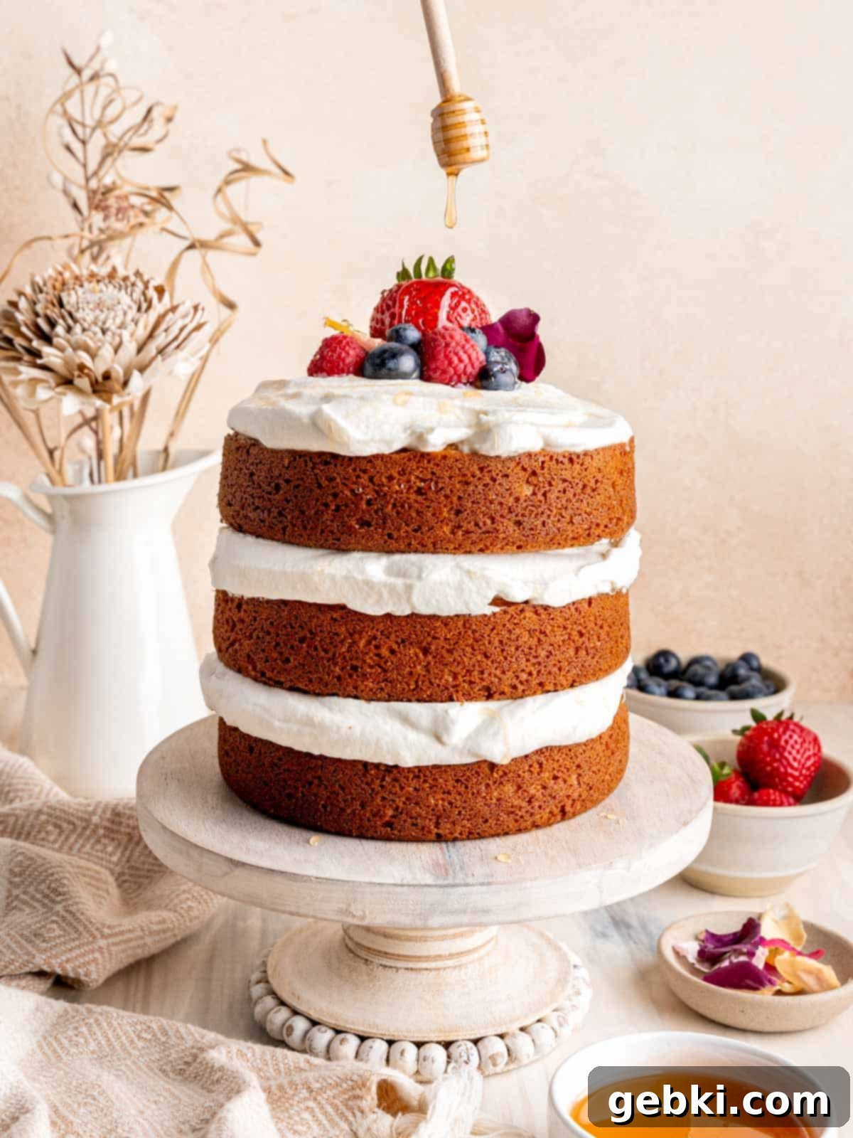 Effortless Honey Vanilla Delight 2 Drizzling honey on top of a honey vanilla layer cake decorated with fresh berries and edible flowers.