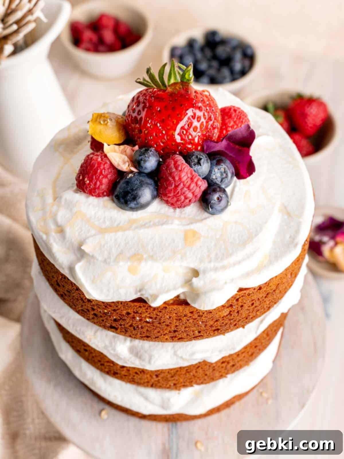 Effortless Honey Vanilla Delight 9 A photo showing the top of a vanilla layer cake decorated with whipped cream, fresh fruit (berries), and a drizzle of honey.