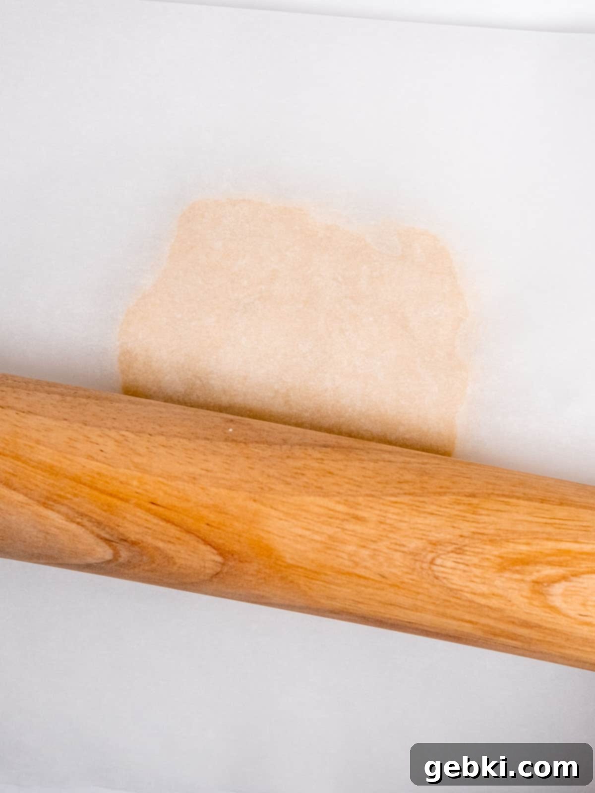 Pressing a rolling pin over pie dough flattened between sheets of parchment paper.