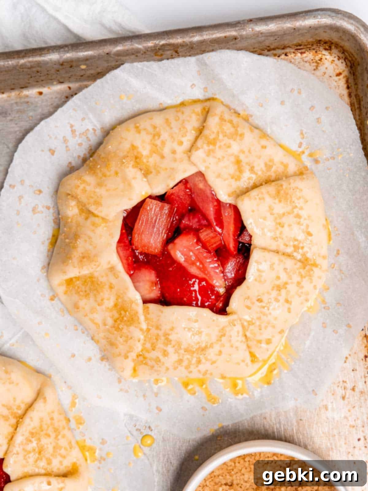 An unbaked strawberry rhubarb galette on a baking sheet with parchment paper.