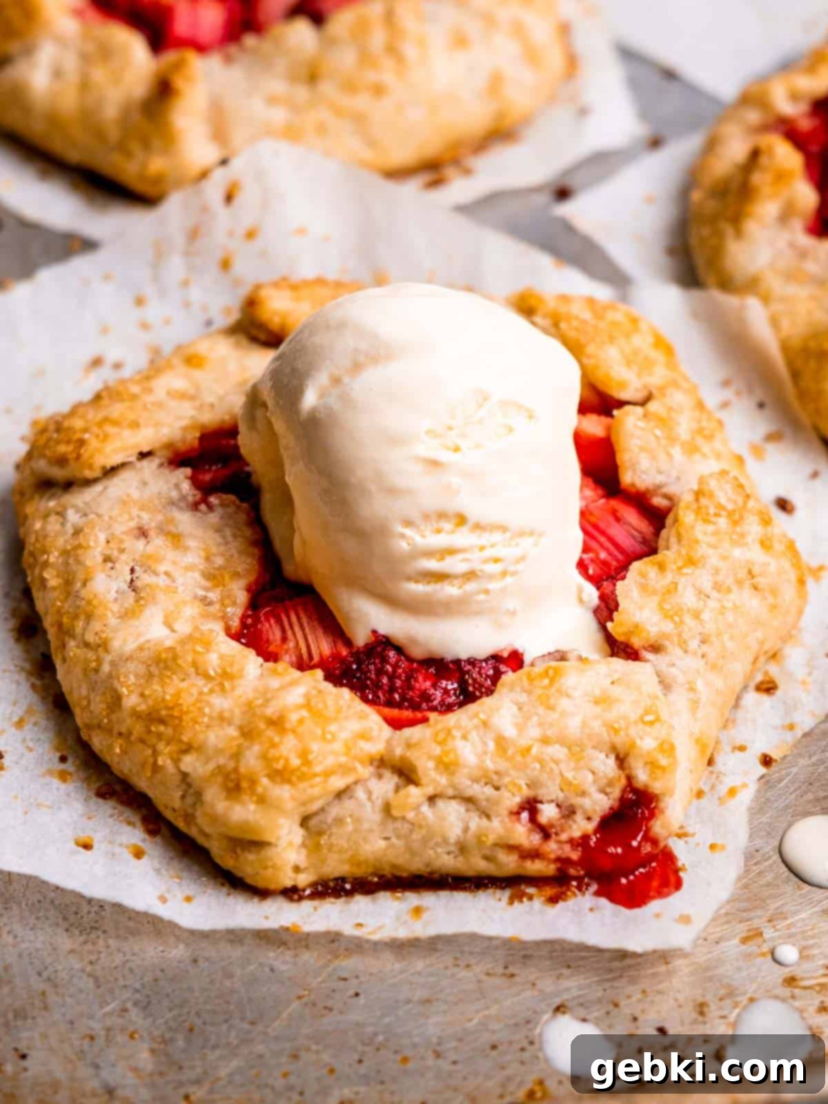 A mini strawberry rhubarb galette with a scoop of vanilla ice cream on top.