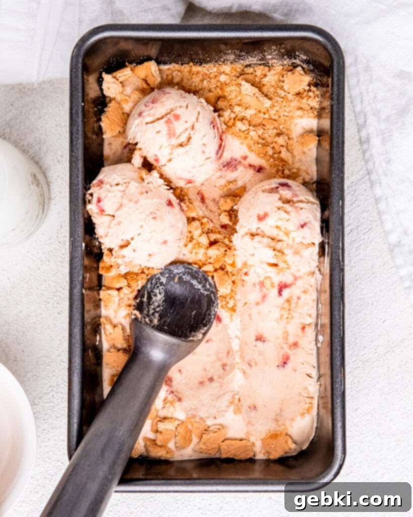 Strawberry Swirl Cheesecake Delight 8 A metal loaf pan full of frozen strawberry cream cheese ice cream topped with crushed graham crackers