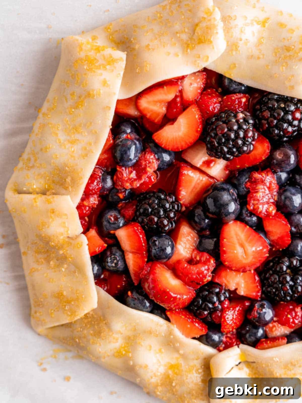 An unbaked berry galette with egg wash and coarse turbinado sugar on the edges, ready for baking.