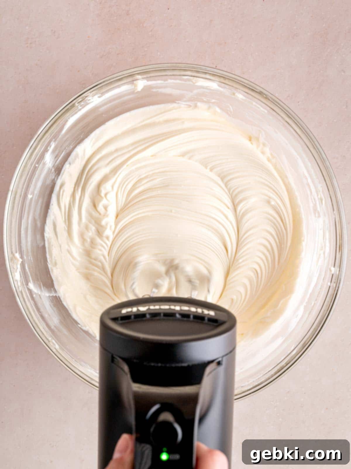 No-Bake Chocolate Cherry Cheesecake 8 Mixing cream cheese with sugar and lemon juice in a bowl with a cordless KitchenAid hand mixer.