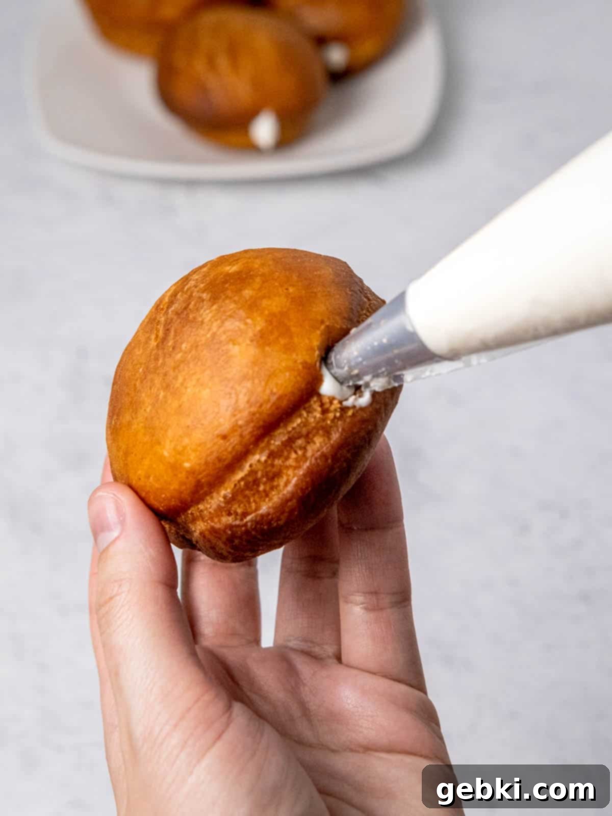 Gooey S'mores Stuffed Donuts 7 A fried donut being filled with fluffy marshmallow cream using a piping bag with a metal tip.