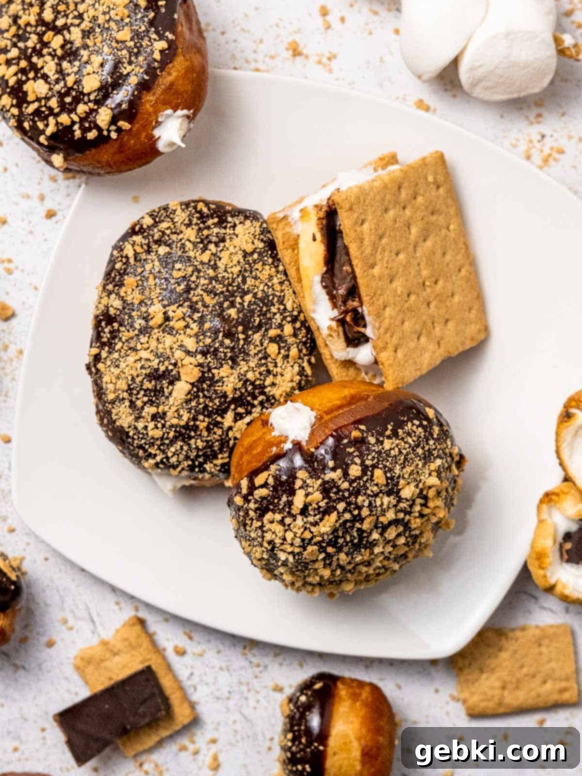 Gooey S'mores Stuffed Donuts 9 A plate of fluffy S'mores donuts topped with chocolate ganache and graham cracker crumbs, alongside a classic s'more on a stick.