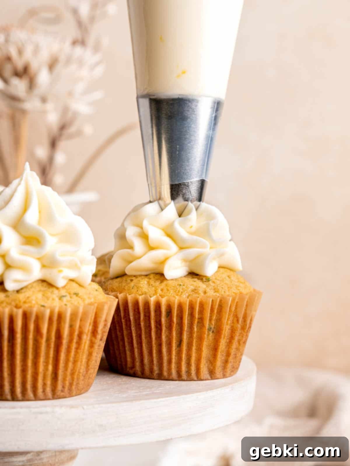 Piping lemon cream cheese frosting onto a lemon zucchini cupcake using a closed star tip.