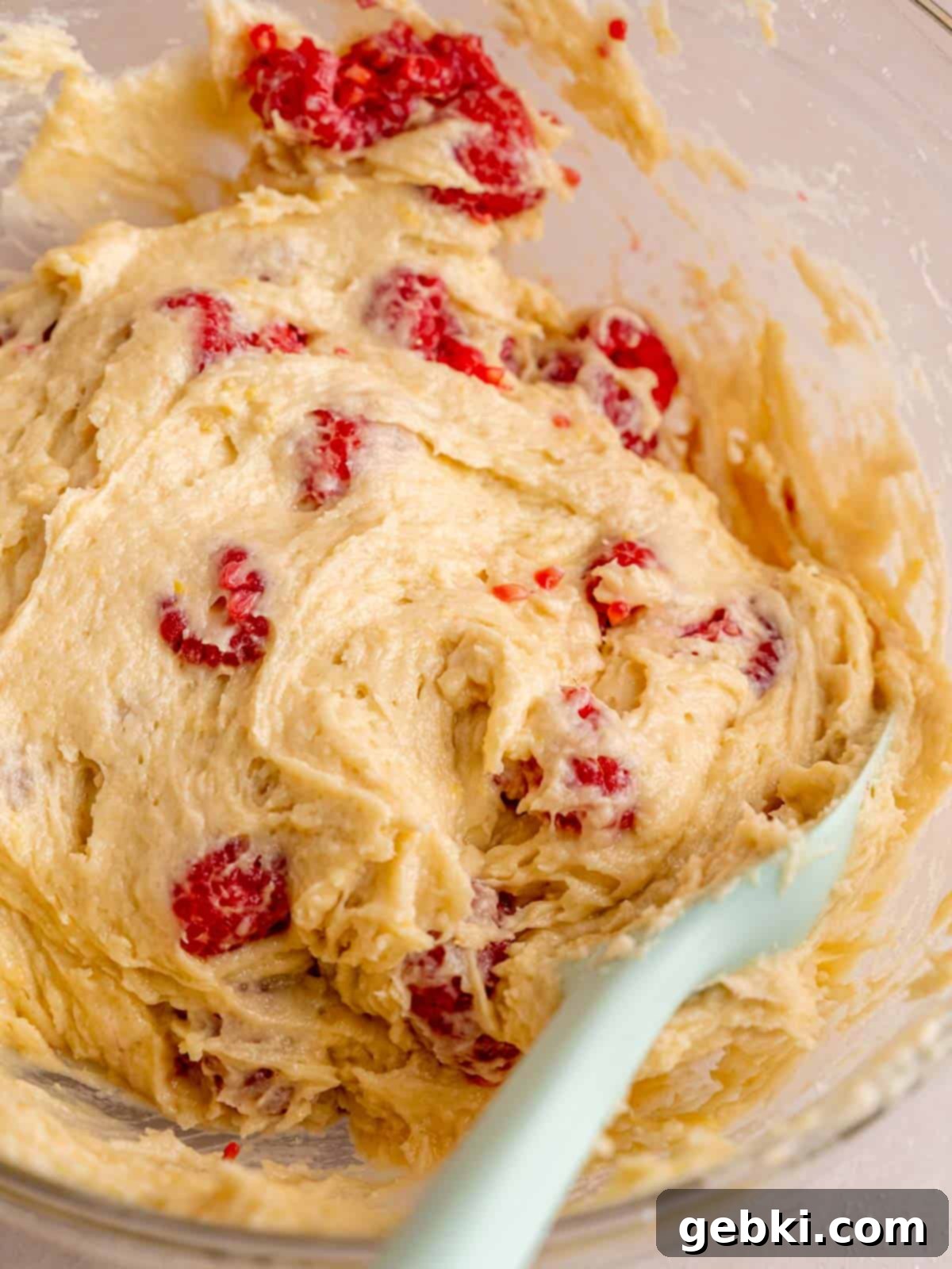 Irresistible Lemon Raspberry Muffins 7 Folding fresh raspberries into lemon muffin batter using a spatula to ensure even distribution.