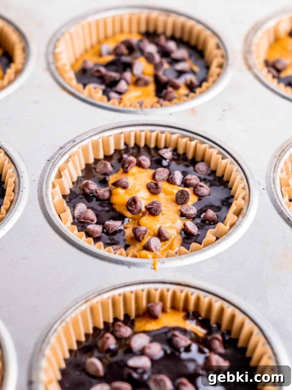 Pumpkin and chocolate muffin batters swirled in muffin liners, ready for baking.