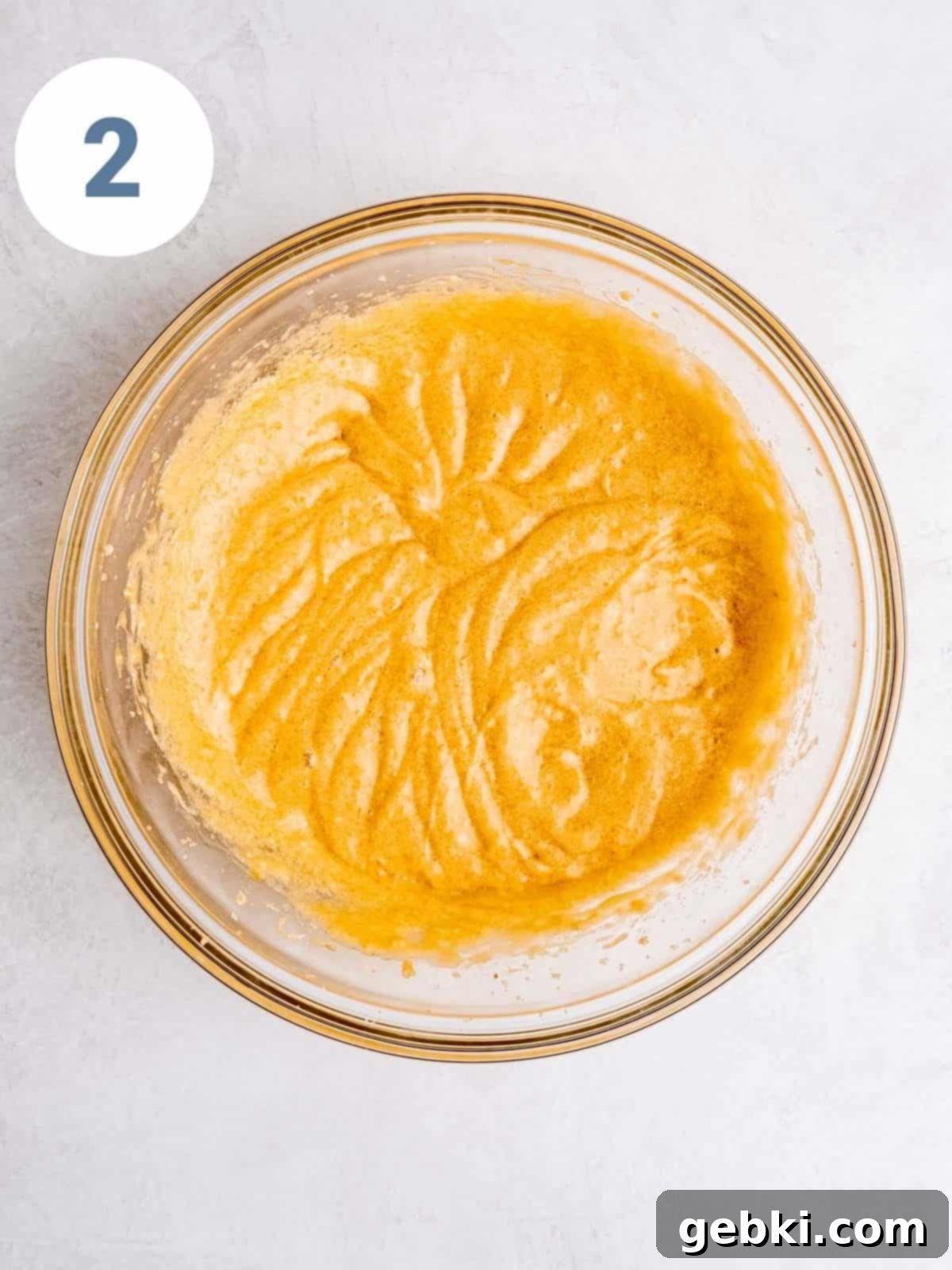 Wet ingredients, including butter, sugars, eggs, vanilla, and applesauce, being mixed in a large bowl with a hand mixer.