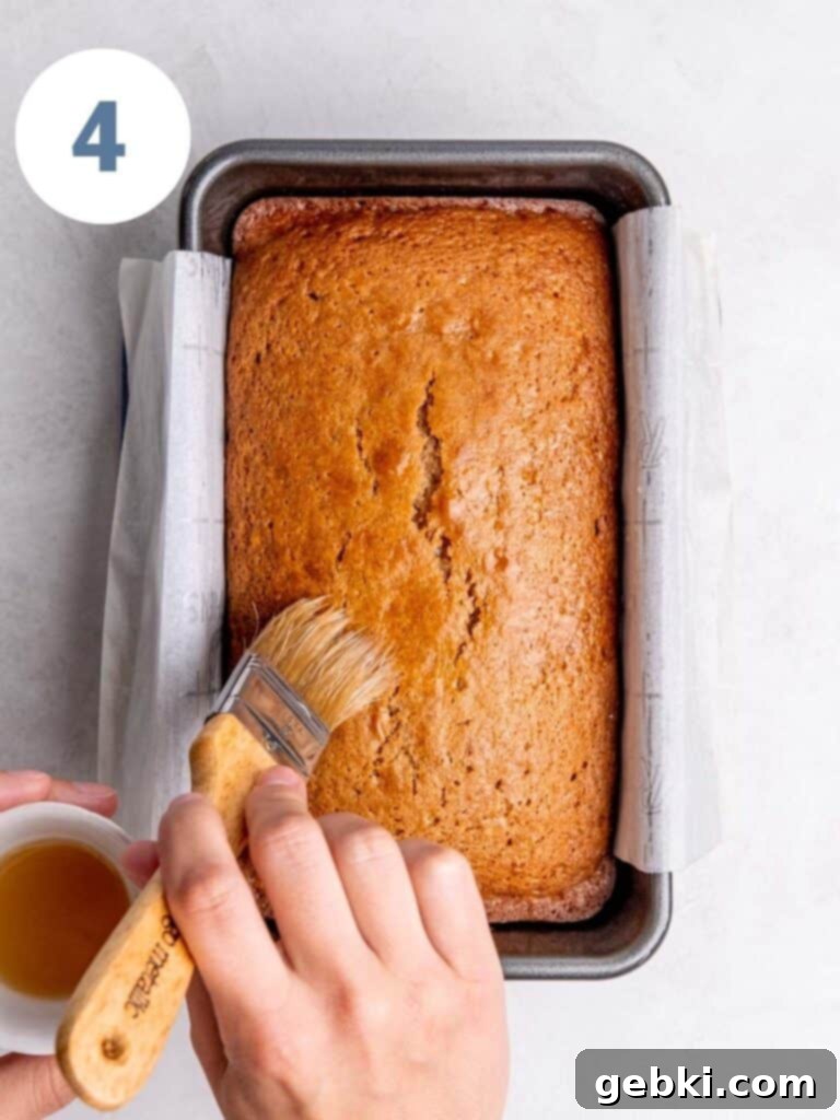 Freshly baked Apple Cider Donut Loaf Cake in a parchment-lined pan, with the top being brushed with apple cider and sprinkled with chai sugar.
