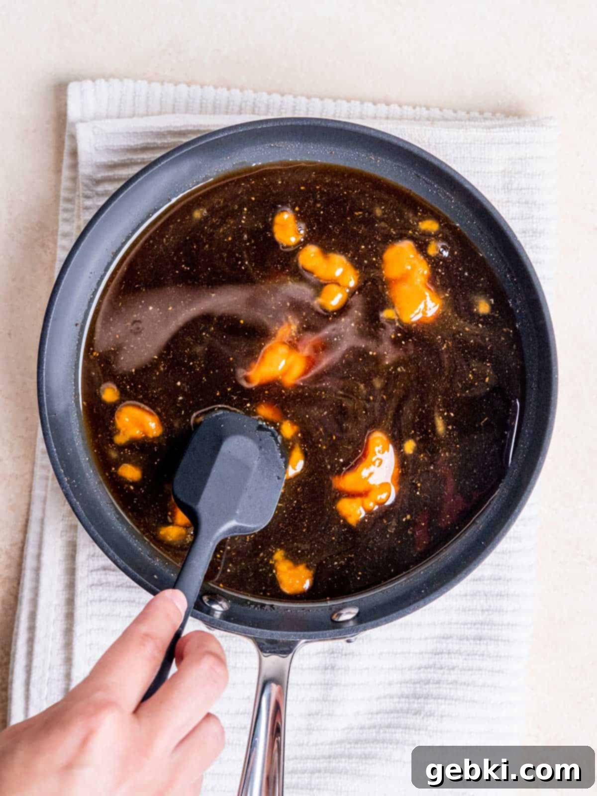 Stirring rich pumpkin puree into the simmering sugar and spice mixture in a pan to create homemade pumpkin spice syrup.