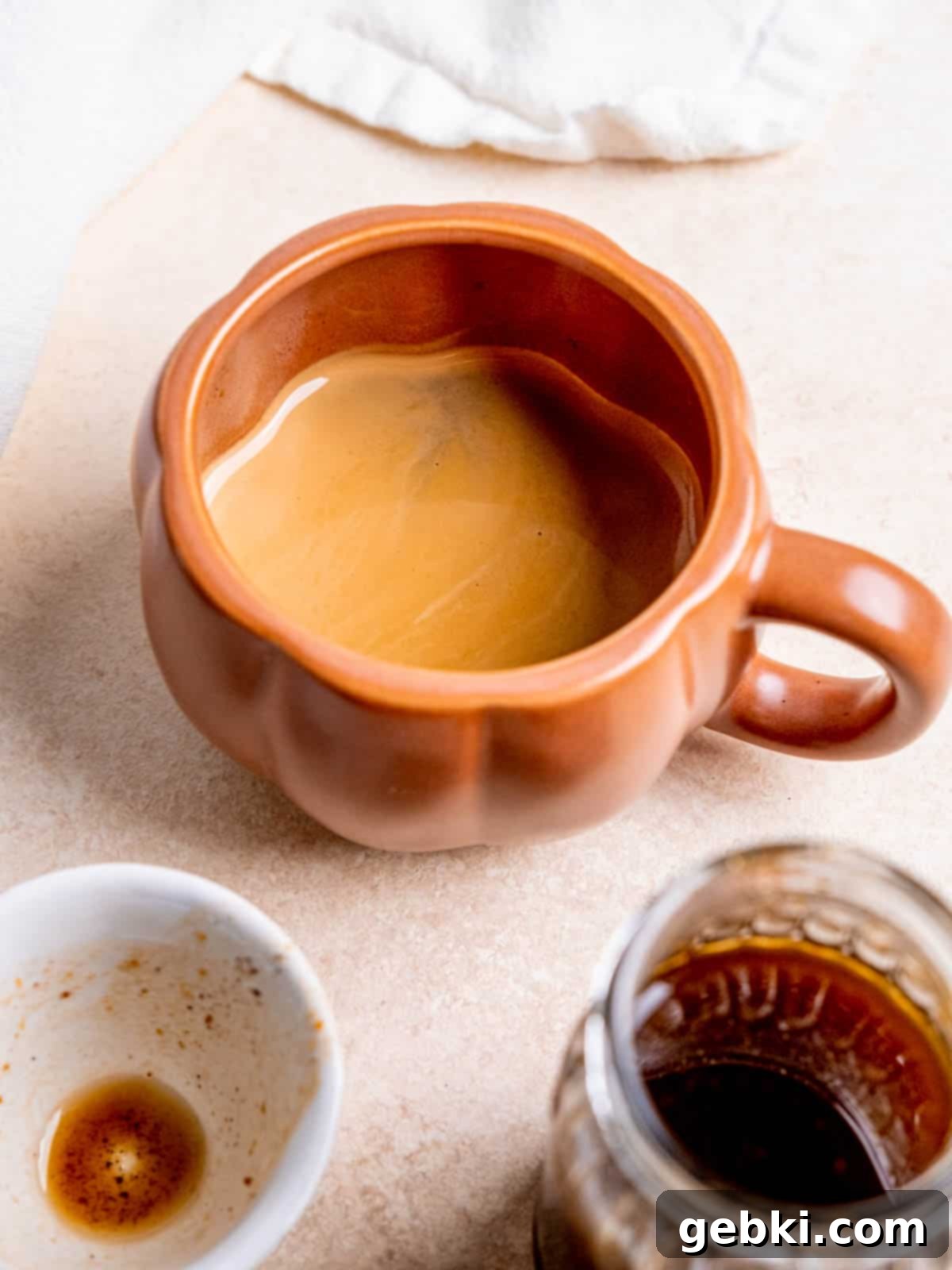 A festive pumpkin-shaped mug filled with dark espresso, ready for the pumpkin spice syrup and milk.