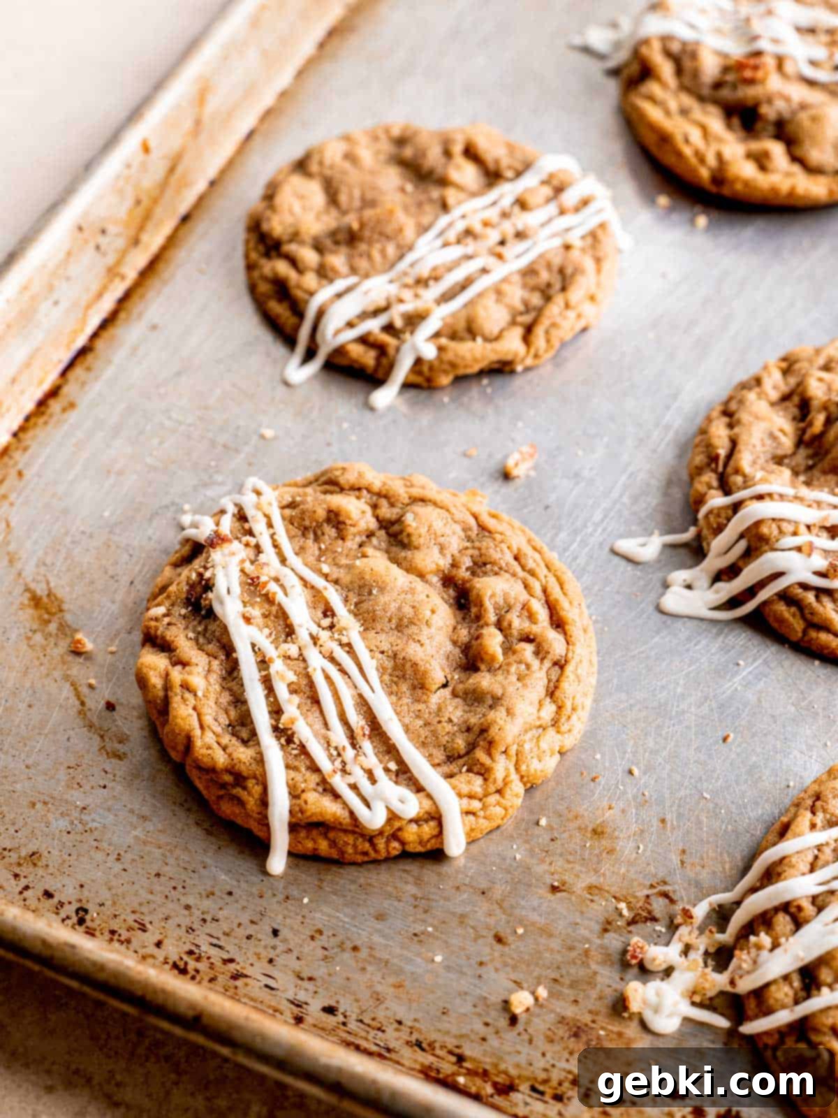 Maple pecan cookies on a baking sheet with cream cheese icing drizzled on top.