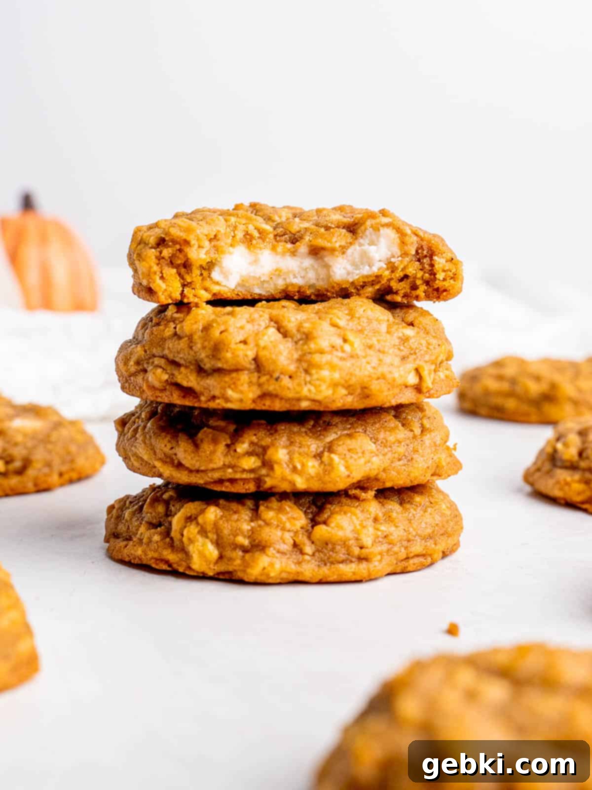 Creamy Pumpkin Cheesecake Oatmeal Cookies 2 A stack of golden-brown oatmeal pumpkin cheesecake cookies with the top one cut in half, revealing the creamy white cheesecake filling inside. The cookies are on a rustic surface, suggesting a warm, inviting fall theme.