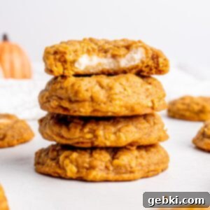 Creamy Pumpkin Cheesecake Oatmeal Cookies 7 A stack of Oatmeal Pumpkin Cheesecake Cookies, with one cut in half to show the creamy filling, against a warm, inviting backdrop.