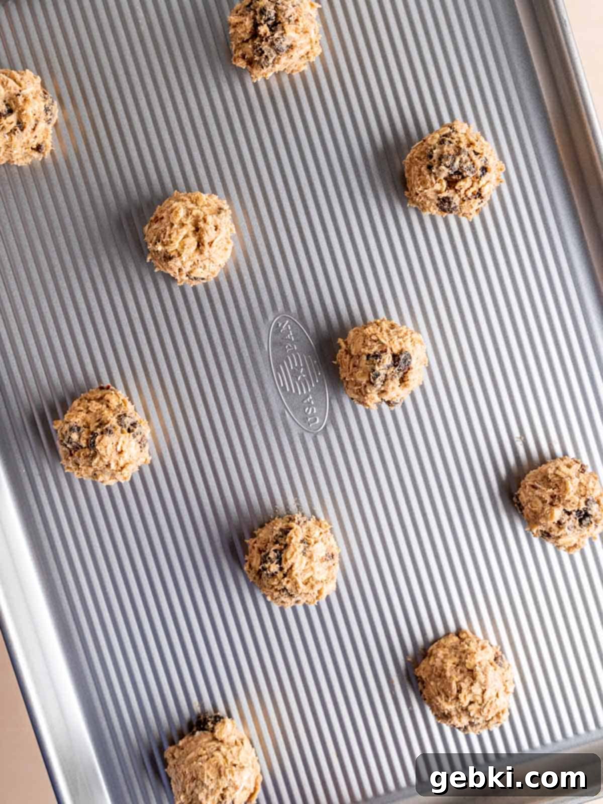 Classic Chewy Oatmeal Raisin Cookies 7 Scooped oatmeal raisin cookie dough balls on a parchment-lined baking sheet, spaced apart.